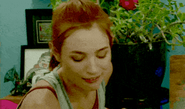 a woman with red hair is smiling in front of a potted plant and a framed picture