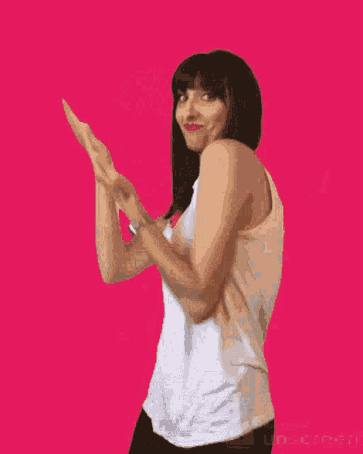 a woman in a white tank top applauds on a pink background