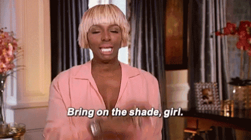 a woman in a pink shirt is standing in a living room and saying `` bring on the shade , girl . ''
