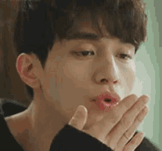 a close up of a young man blowing a kiss with his hand .