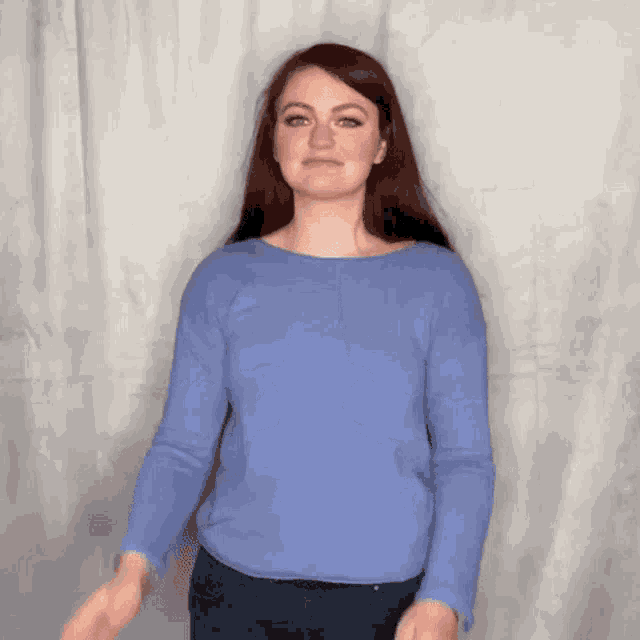 a woman wearing a blue sweater and jeans is making a funny face .