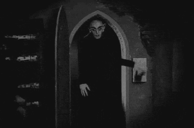 a black and white photo of a vampire standing in an archway .