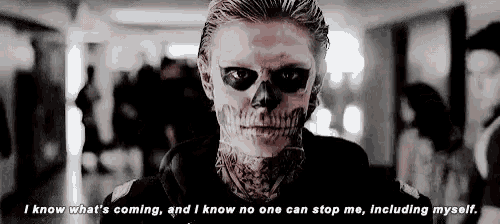a man with a skull painted on his face is standing in a hallway with a quote .
