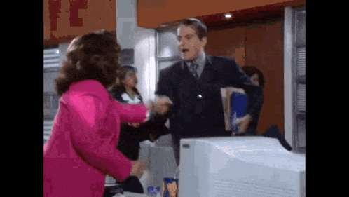 a woman in a pink jacket is shaking hands with a man in a suit .