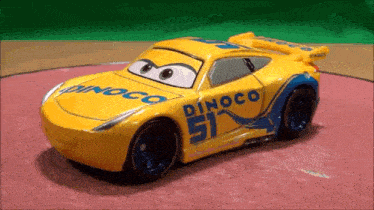 a yellow toy car with the number 51 on it is sitting on a red surface .