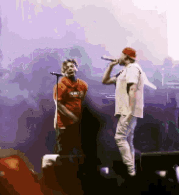 a man singing into a microphone with another man standing behind him