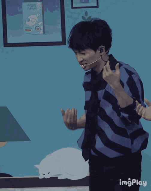 a man in a blue and black striped shirt is dancing in front of a blue wall with a cat on it