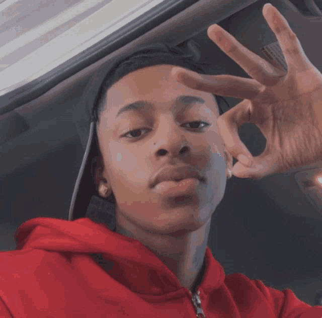 a young man wearing a red hoodie and a black hat is giving a peace sign