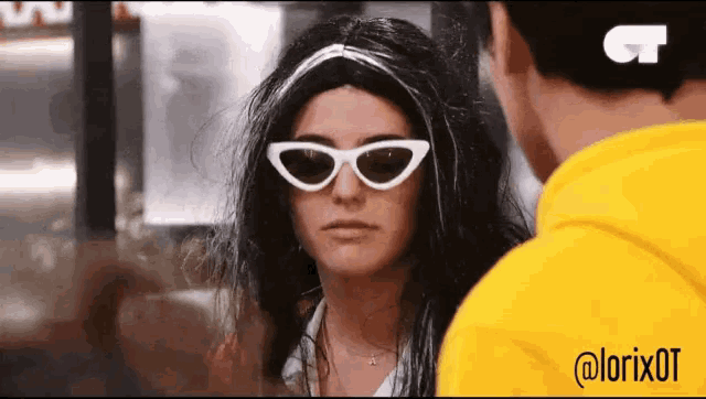 a woman wearing a wig and sunglasses is looking at a man in a yellow hoodie