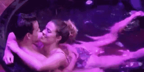 a man and a woman are kissing in a jacuzzi filled with purple lights .