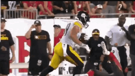 a football player is running with the ball on a field while a referee looks on .