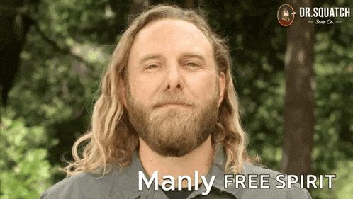 a man with long hair and a beard is smiling with the words manly free spirit below him