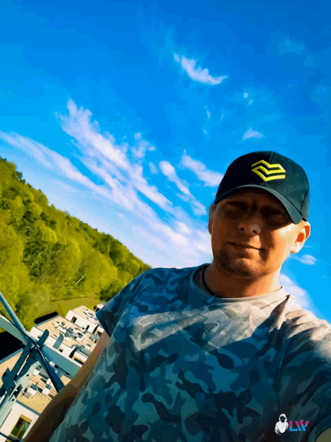 a man wearing a black hat with a yellow triangle on it stands in front of a blue sky