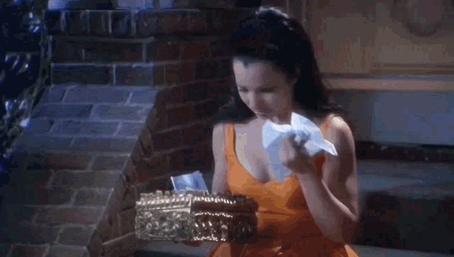 a woman in an orange dress is holding a box of tissues in her hand .