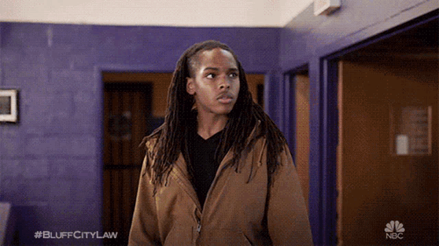 a man with dreadlocks is standing in front of a purple wall with #bluffcitylaw written on the bottom right