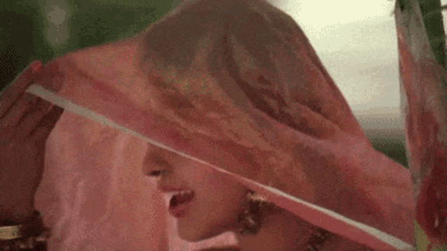 a woman in a pink dress is covering her face with a pink scarf .
