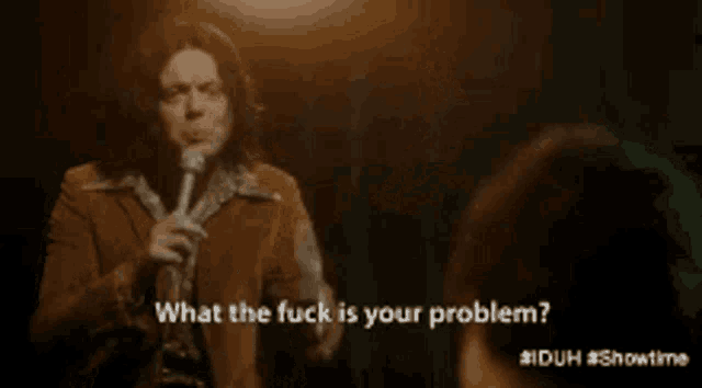 a man singing into a microphone with the words what the fuck is your problem behind him