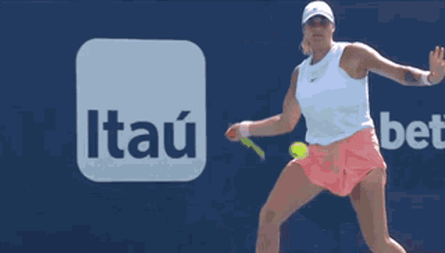 a woman playing tennis in front of a itau logo