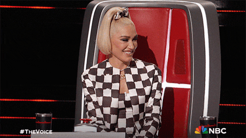 a woman in a black and white checkered jacket is sitting in a chair with nbc written on the back