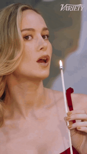 a woman is holding a lit candle in front of a variety sign