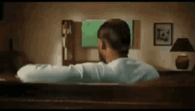 a man is sitting in a bathtub watching a green screen tv .