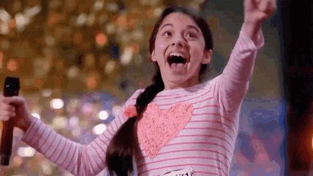 a young girl is singing into a microphone with her mouth open and her arms in the air .