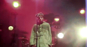 a man in a green coat is singing into a microphone on stage