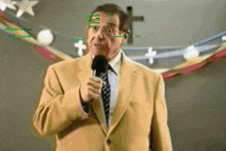 a man in a suit and tie speaking into a microphone with a cross in the background