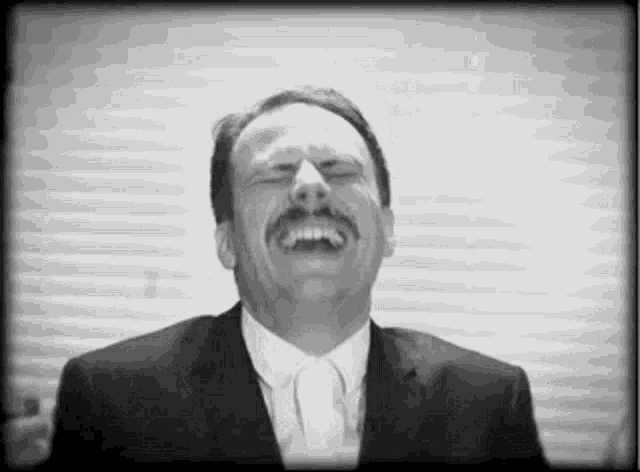 a black and white photo of a man in a suit and tie laughing .