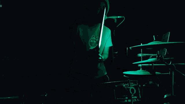 a man playing drums in a dark room with a green light