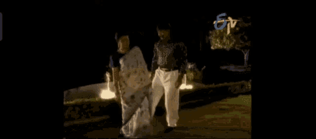 a man and a woman are standing next to each other in front of a fountain at night .