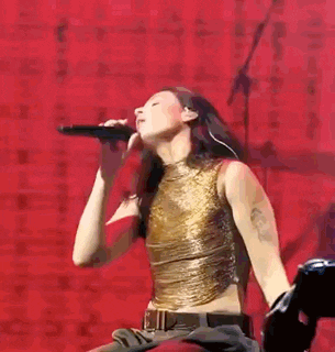 a woman in a gold tank top is singing into a microphone on a stage .