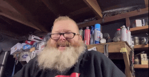 a man with glasses and a beard is smiling in front of a shelf with ziploc bags on it