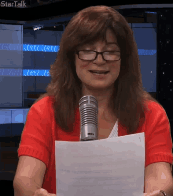 a woman wearing glasses is holding a piece of paper in front of a microphone with startalk written in the background