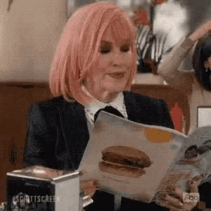 a woman with pink hair is reading a magazine with a picture of a hamburger .