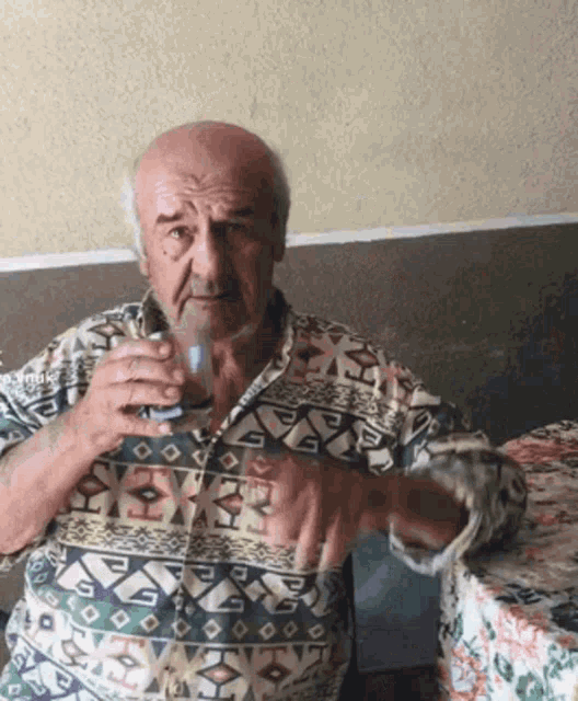 a man in a colorful shirt is sitting at a table drinking a glass of water