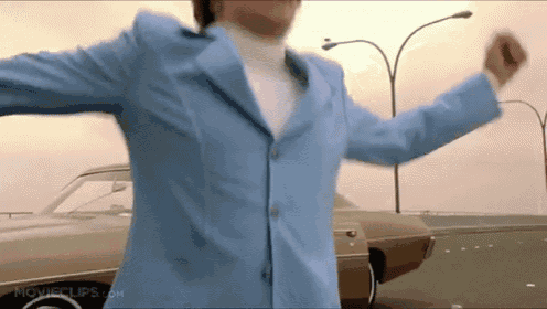 a man in a blue suit is dancing in front of a car