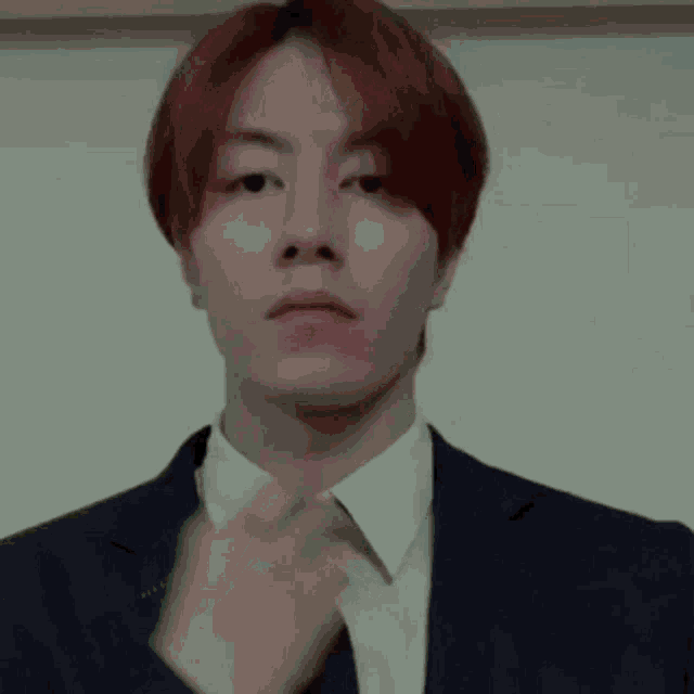 a young man with red hair is wearing a suit and tie and adjusting his tie .