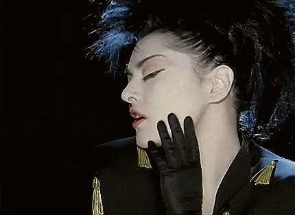 a woman wearing a black jacket has red beads hanging from her ears