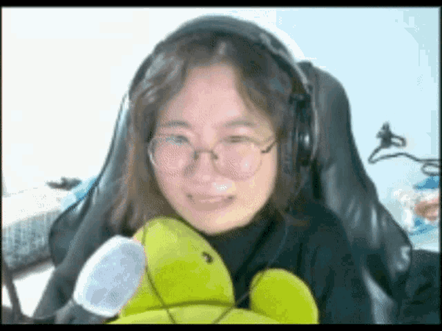 a woman wearing headphones and glasses is holding a stuffed turtle .