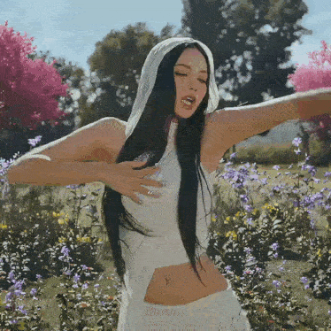 a woman in a white dress is standing in a field of flowers with her arms outstretched