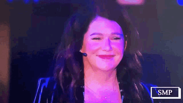a woman with a microphone in her ear is smiling in front of a sign that says smp