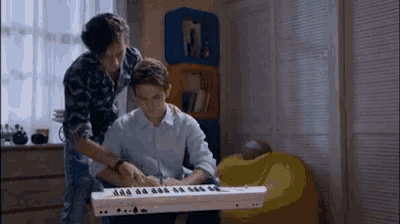 a man is helping another man play a keyboard .