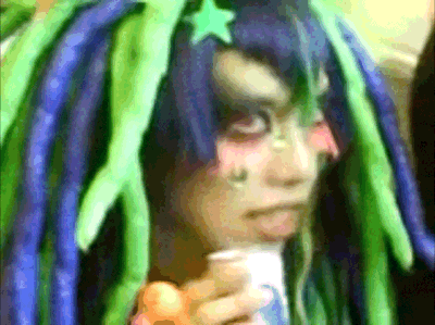 a person with blue and green dreadlocks holds a cup