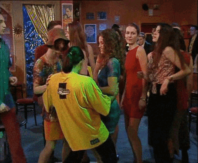 a group of people are dancing in a room and one of them is wearing a yellow shirt with a duck on the front
