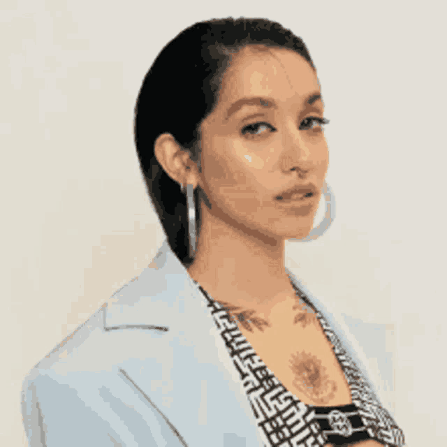 a woman with a tattoo on her chest is wearing a blue jacket and earrings