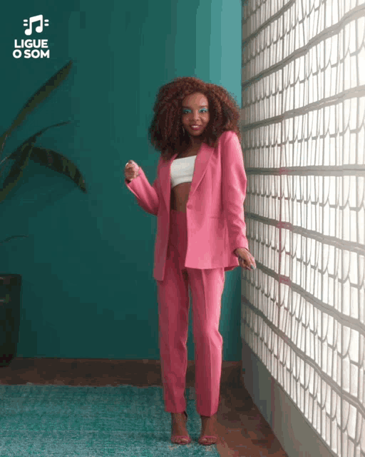 a woman in a pink suit stands in front of a blue wall with the words " ligue o som " on it