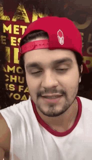 a man with a beard wearing a red hat and a white tank top