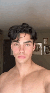a shirtless young man is taking a selfie in a room with pictures on the wall .