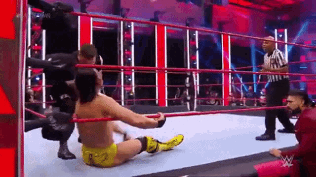 a wrestler is laying on the floor in a wrestling ring while a referee looks on .